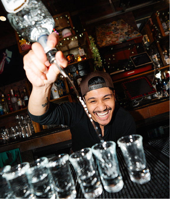 Smiling bartender pouring a round of shots behind a Warehouse bar.