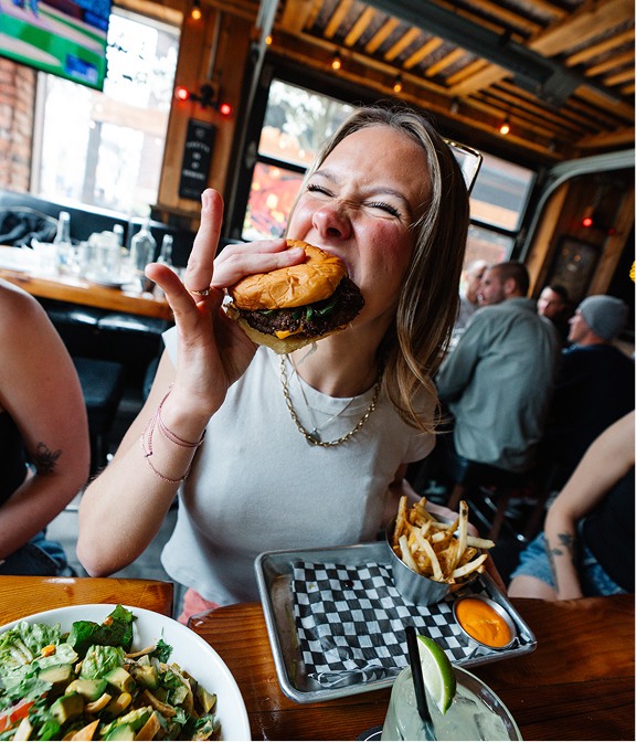 Guest eating a burger with fries, salad, and drinks at a Warehouse table.