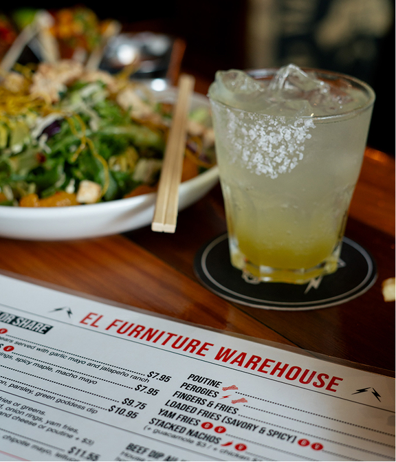 Cocktail served beside the El Furniture Warehouse menu and share plates.