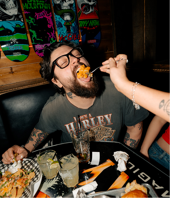 Guest being fed a bite of food while seated with drinks and share plates at Warehouse.