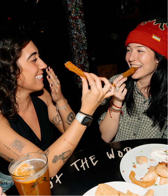 Friends laughing while sharing fried appetizers and drinks at Warehouse.