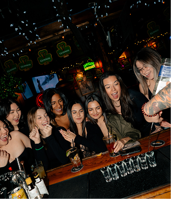 Group of friends laughing at the bar as a bartender pours shots at Warehouse.