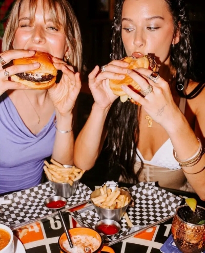 Burger lovers indulging in juicy burgers and fries at Warehouse, surrounded by dipping sauces and cocktails.