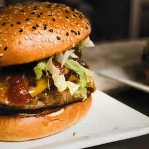 Juicy sesame-seed bun burger with cheddar, lettuce, tomato, and sauce served at El Furniture Warehouse.
