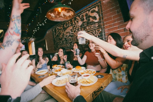 Group raising drinks and sharing burgers, nachos, and pasta at a packed, energetic Warehouse table.