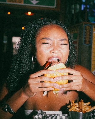 A smiling customer savoring a juicy burger at Warehouse with a side of crispy fries and a refreshing beer.