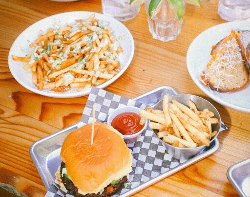 Stacked burger, golden fries, loaded cheesy fries, and grilled cheese served on wood table at El Furniture Warehouse Vancouver.