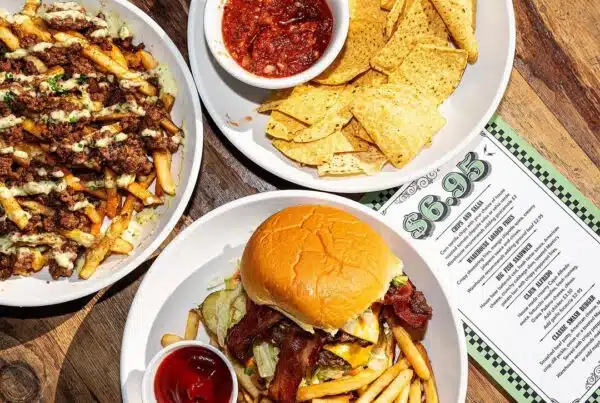 Overhead shot of bacon cheeseburger with fries, loaded fries with jalapeño sauce, and chips with salsa beside the $6.95 Happy Hour Menu.