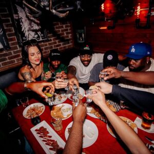 Group of friends raising shots over a loaded table of late-night eats at Warehouse, ready to kick off the after-party.