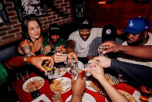 Group of friends raising shots over a loaded table of late-night eats at Warehouse, ready to kick off the after-party.