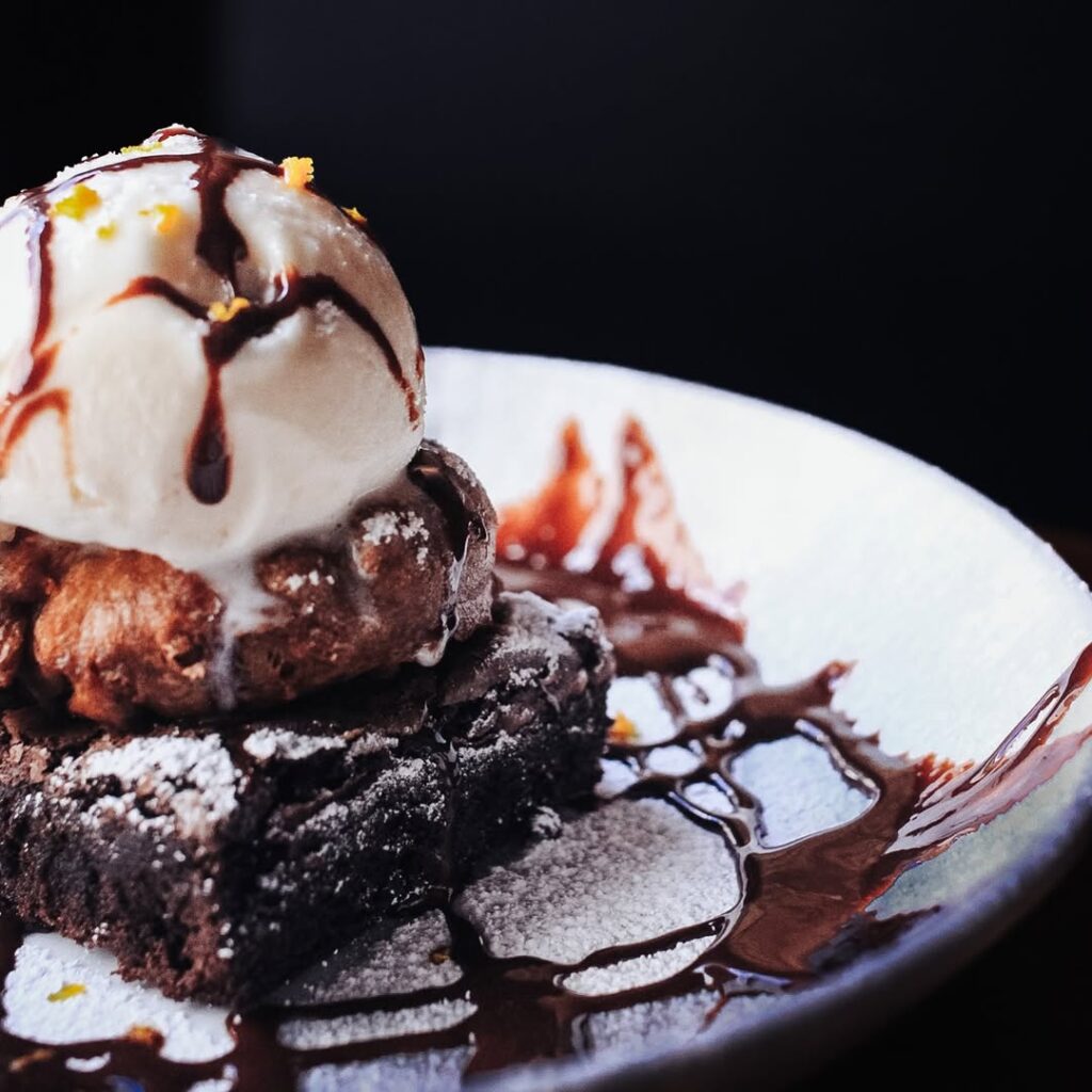 Decadent brownie dessert topped with ice cream, chocolate drizzle, and powdered sugar at Warehouse.
