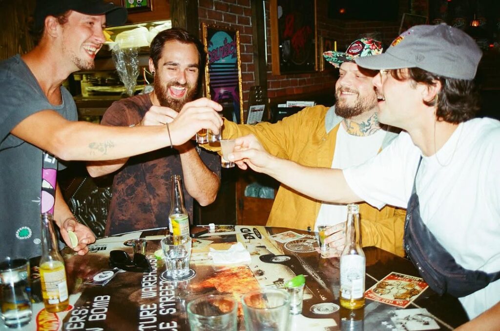 Group of friends laughing and clinking shot glasses around a sticker-covered pub table at Warehouse.