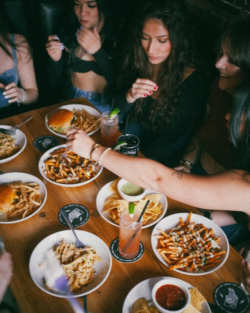 Group of friends sharing loaded fries, burgers, nachos, and drinks during a lively meal at Warehouse.