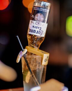 A Corona Extra beer bottle inverted into a sugared-rim glass with a straw, creating a playful and eye-catching cocktail presentation.