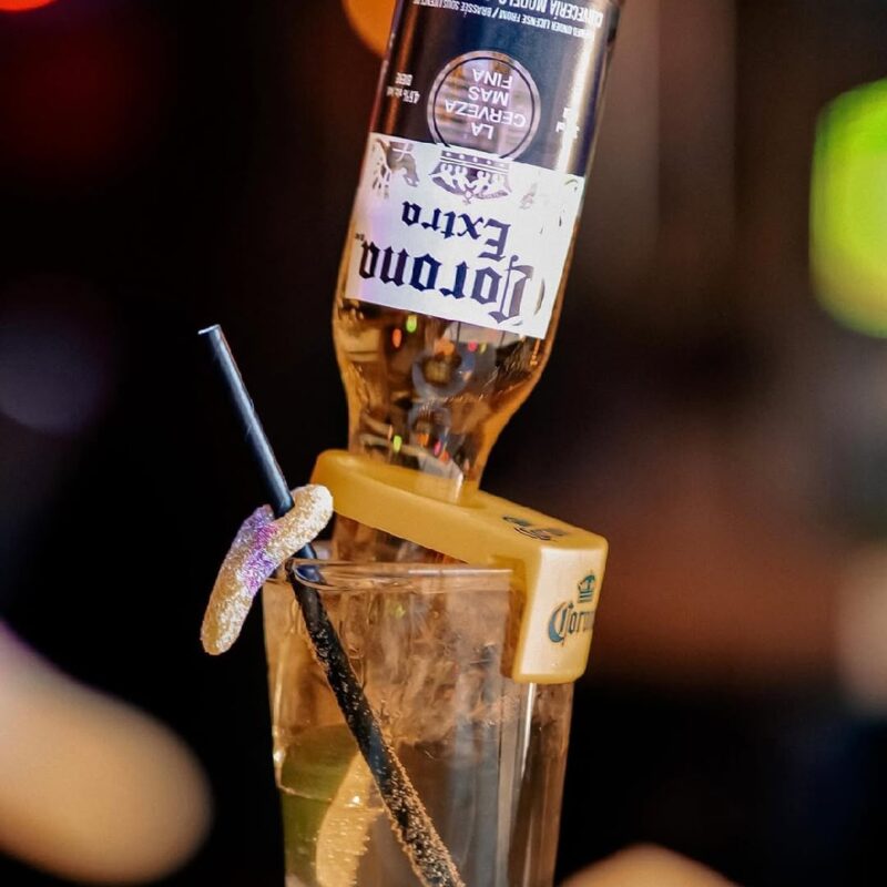 A Corona Extra beer bottle inverted into a sugared-rim glass with a straw, creating a playful and eye-catching cocktail presentation.