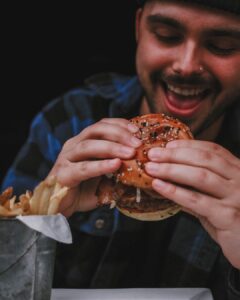 Man holding a stacked Signature Warehouse burger with a big smile.