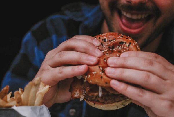 Man holding a stacked Signature Warehouse burger with a big smile.