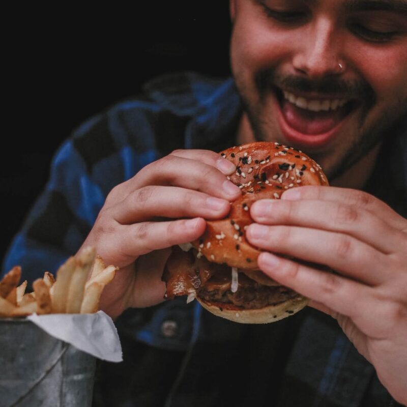 Man holding a stacked Signature Warehouse burger with a big smile.