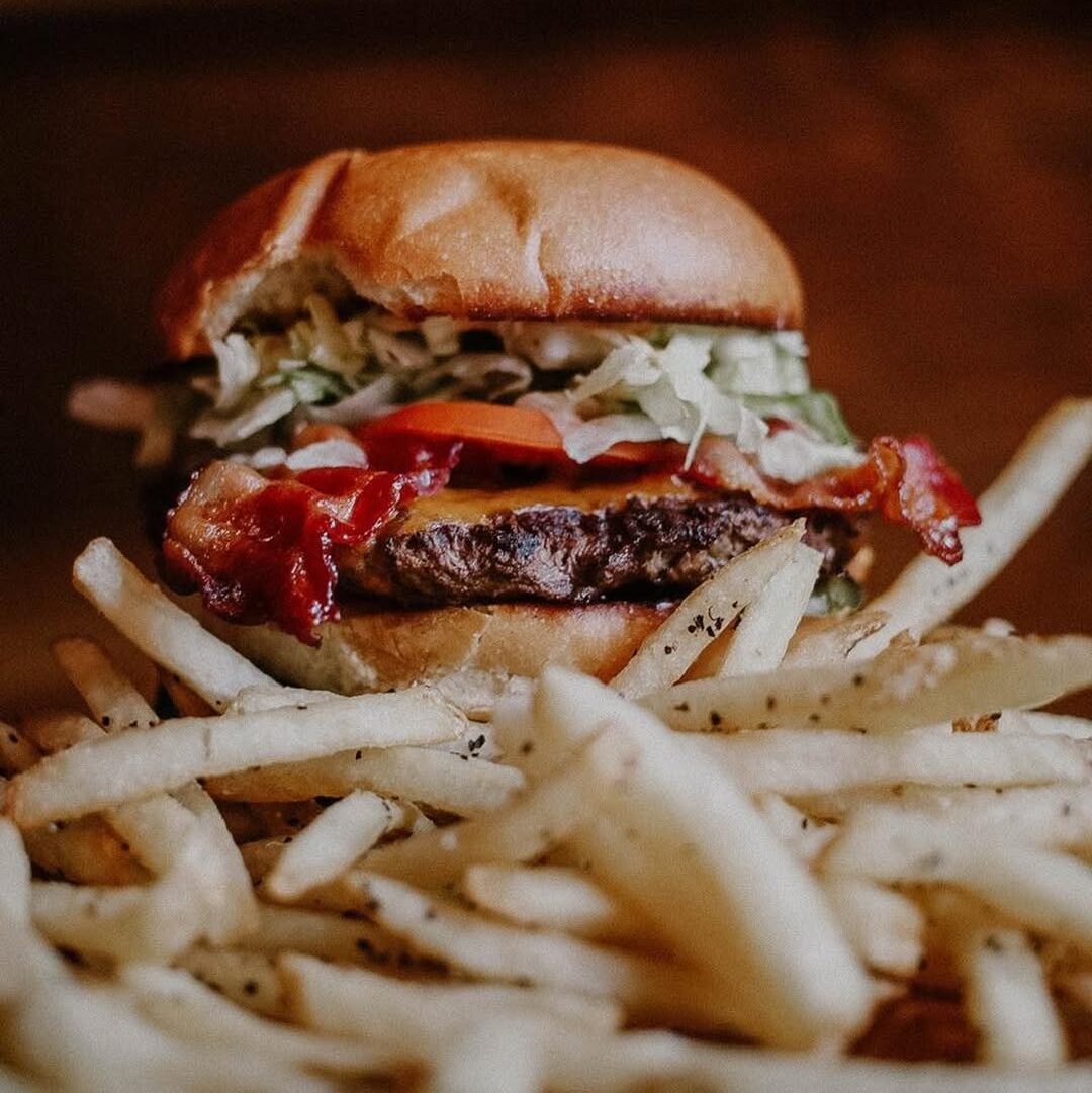A Warehouse classic burger with a crispy beef patty, cheese slice, fresh coleslaw, and crispy bacon, served with a side of fries.