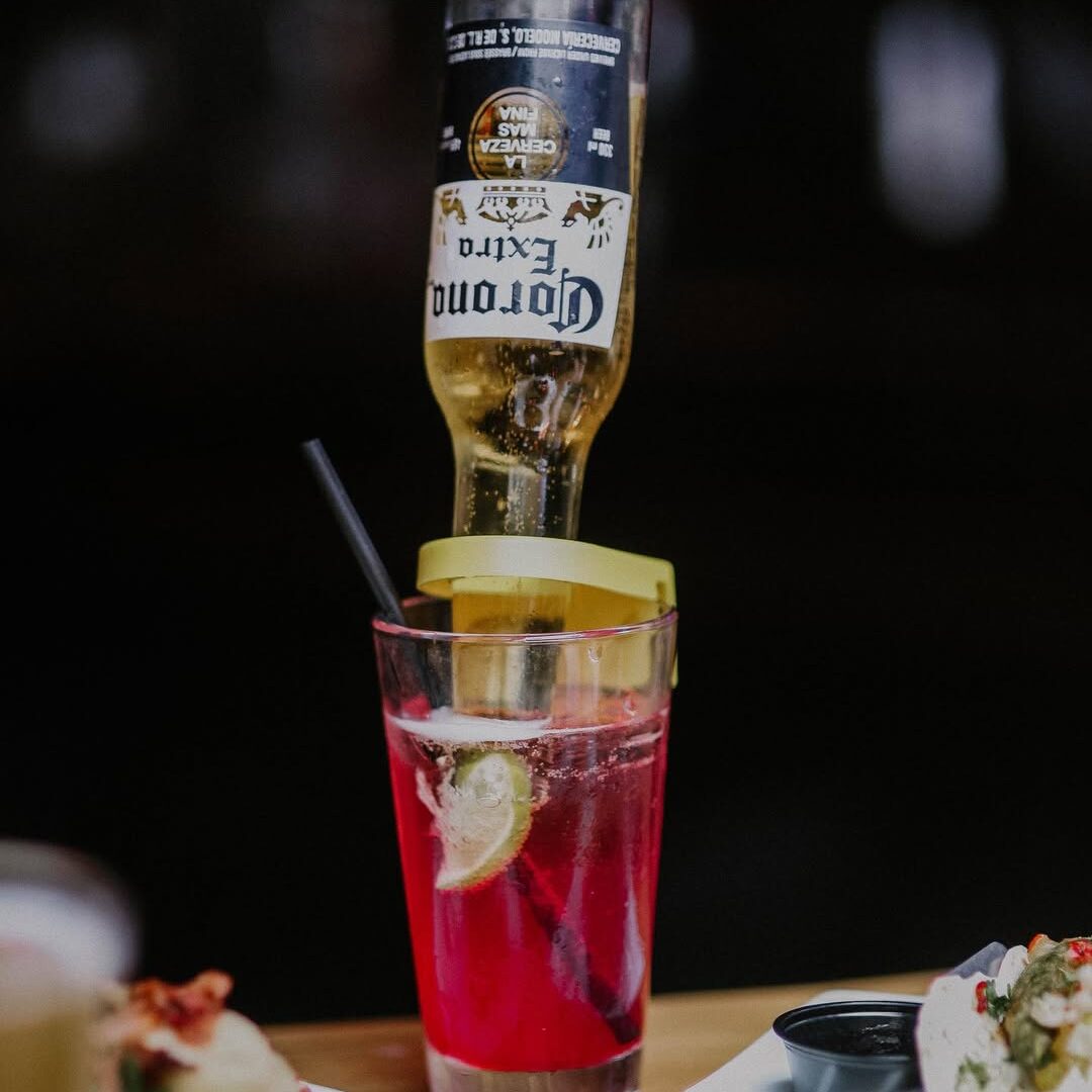 Close-up of the Pink Warehouse cocktail, featuring a flipped Corona bottle in a pink-hued drink garnished with lime.