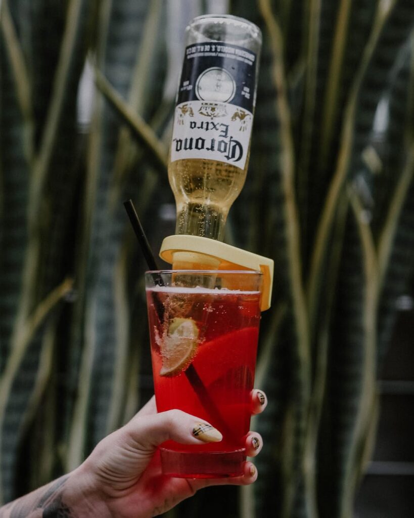 "The Pink Warehouse" cocktail with lime wedge and upside-down Corona Extra bottle.