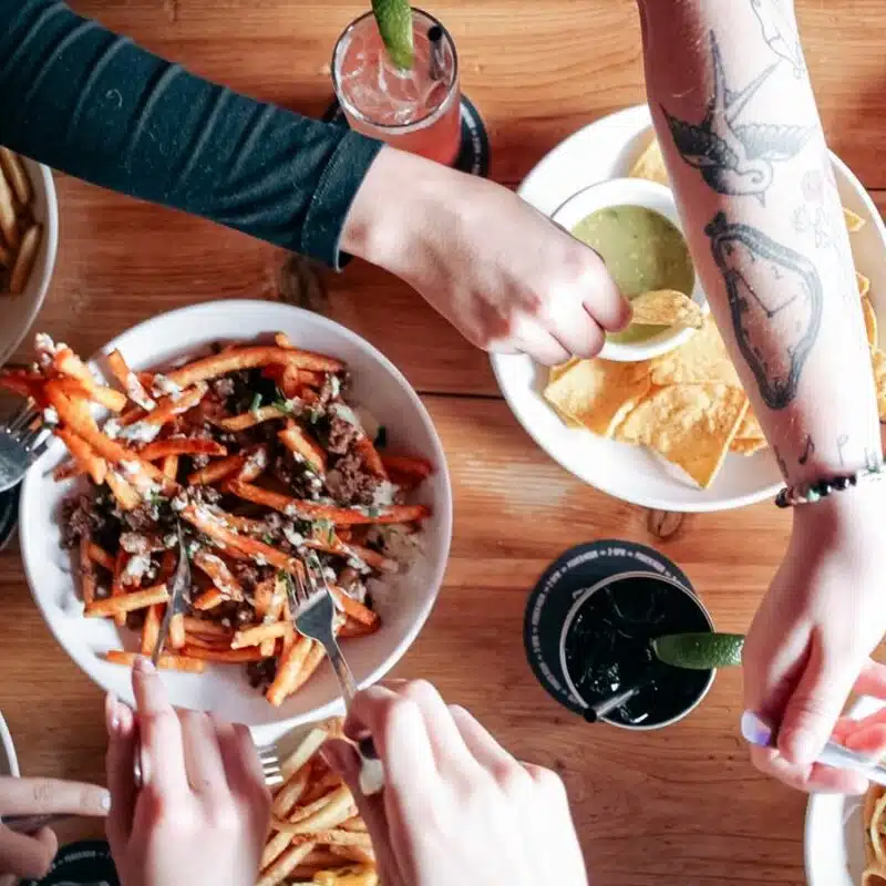 A table filled with food, a bowl of Poutine being shared along with nachos and fries at Warehouse.