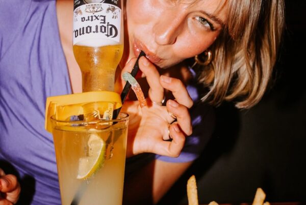 Woman sipping a Warehouse Keyrona cocktail, served with a basket of golden fries, inside the lively Stephen Ave location.