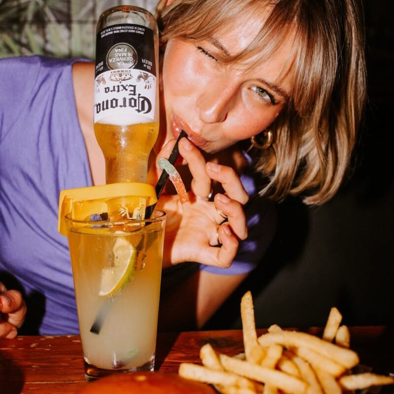 Woman sipping a Warehouse Keyrona cocktail, served with a basket of golden fries, inside the lively Stephen Ave location.