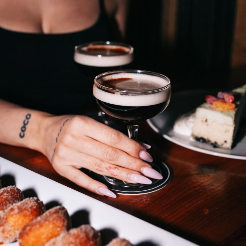 A plate of mini-donuts and a server placing some cocktails on a table at Warehouse.