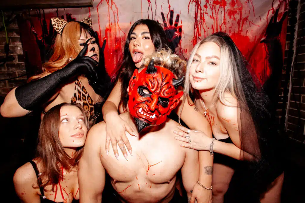 Group of friends in Halloween costumes posing at The Warehouse’s spooky party with red devil masks and horror-themed décor.