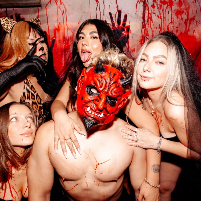 Group of friends in Halloween costumes posing at The Warehouse’s spooky party with red devil masks and horror-themed décor.