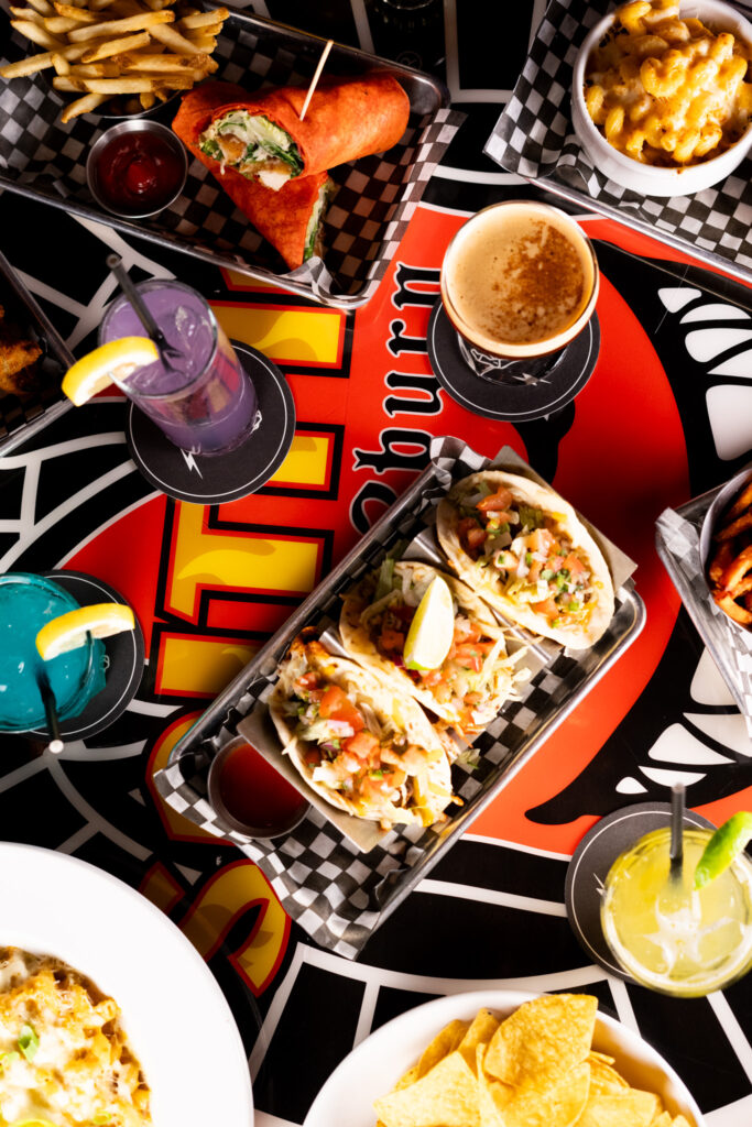 A colorful spread of tacos, wraps, fries, mac and cheese, and cocktails on a vibrant Warehouse Seattle table during game night.