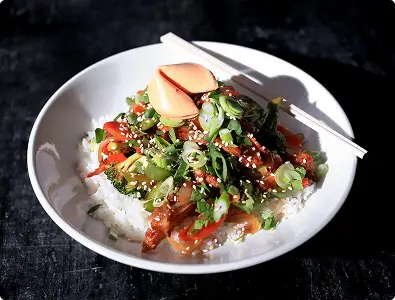 A close-up of a poke bowl with rice, fish, and various toppings in a white bowl.