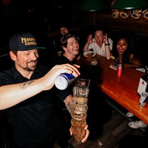Bartender stacking and pouring drinks as friends laugh and cheer at Warehouse Calgary.