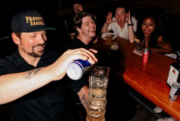 Bartender stacking and pouring drinks as friends laugh and cheer at Warehouse Calgary.