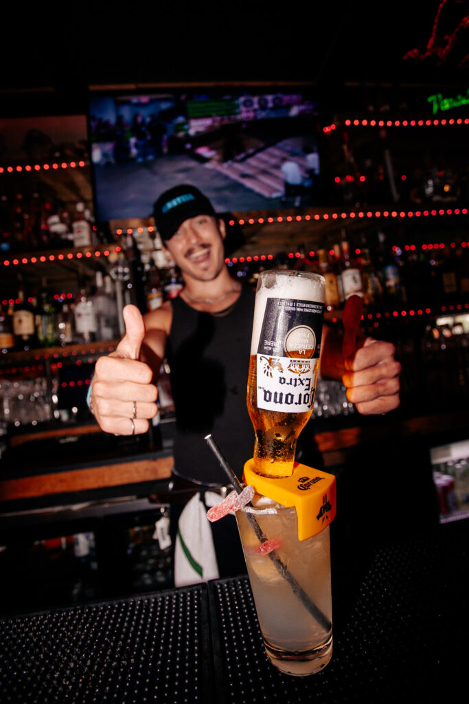 A smiling bartender at Warehouse giving a thumbs-up behind the bar with a cocktail in front of him.