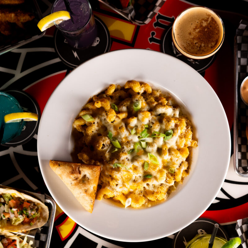 An overhead shot of a large bowl of cheesy mac and cheese surrounded by cocktails, tacos, and bar snacks at Warehouse.
