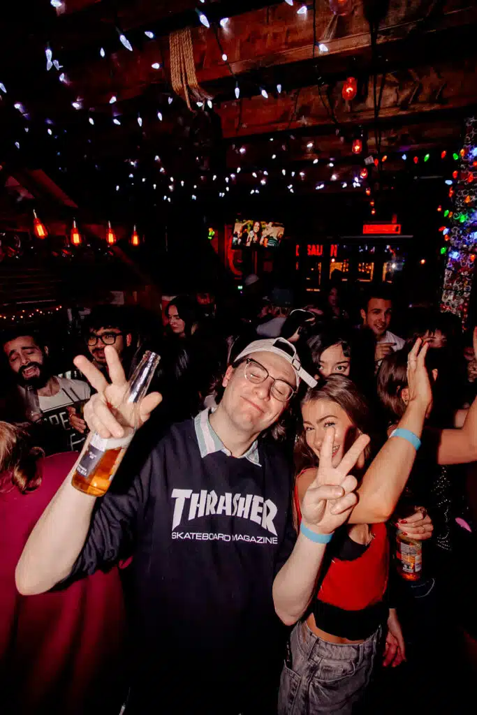 Friends dancing at Warehouse, holding beer bottles and flashing peace signs during a late-night party.