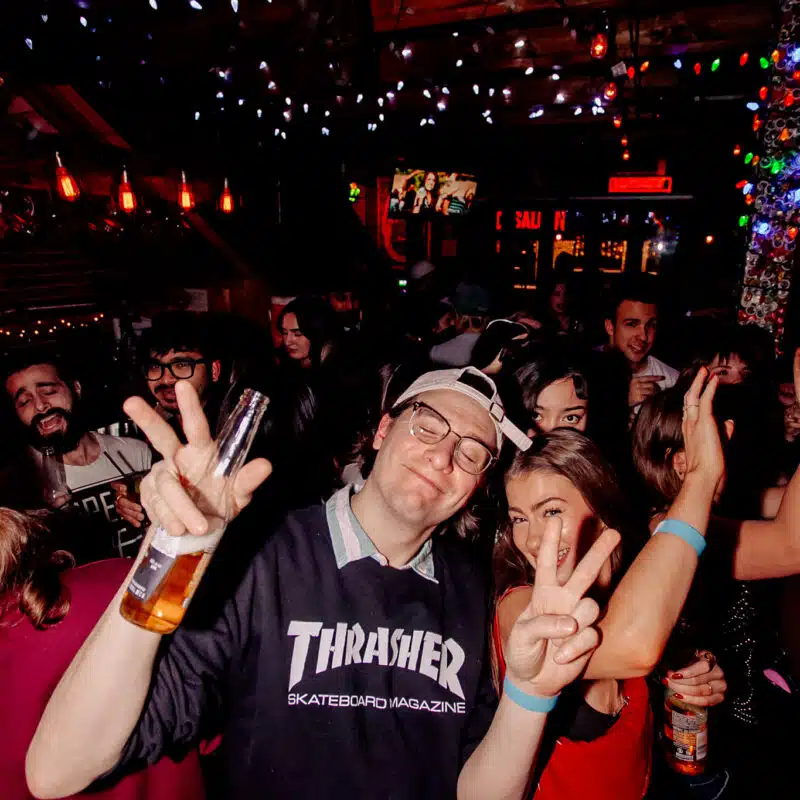 Friends dancing at Warehouse, holding beer bottles and flashing peace signs during a late-night party.