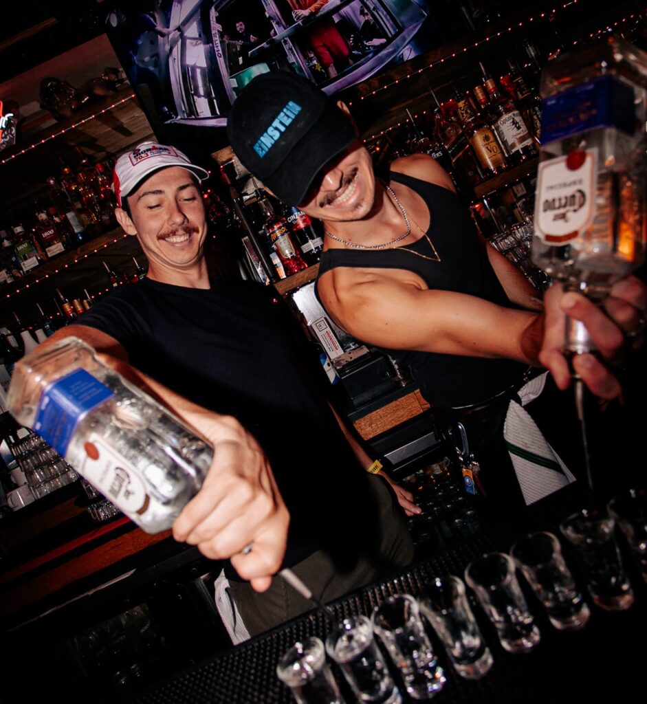 The bartenders at Warehouse are pouring Vodka into shot glasses.