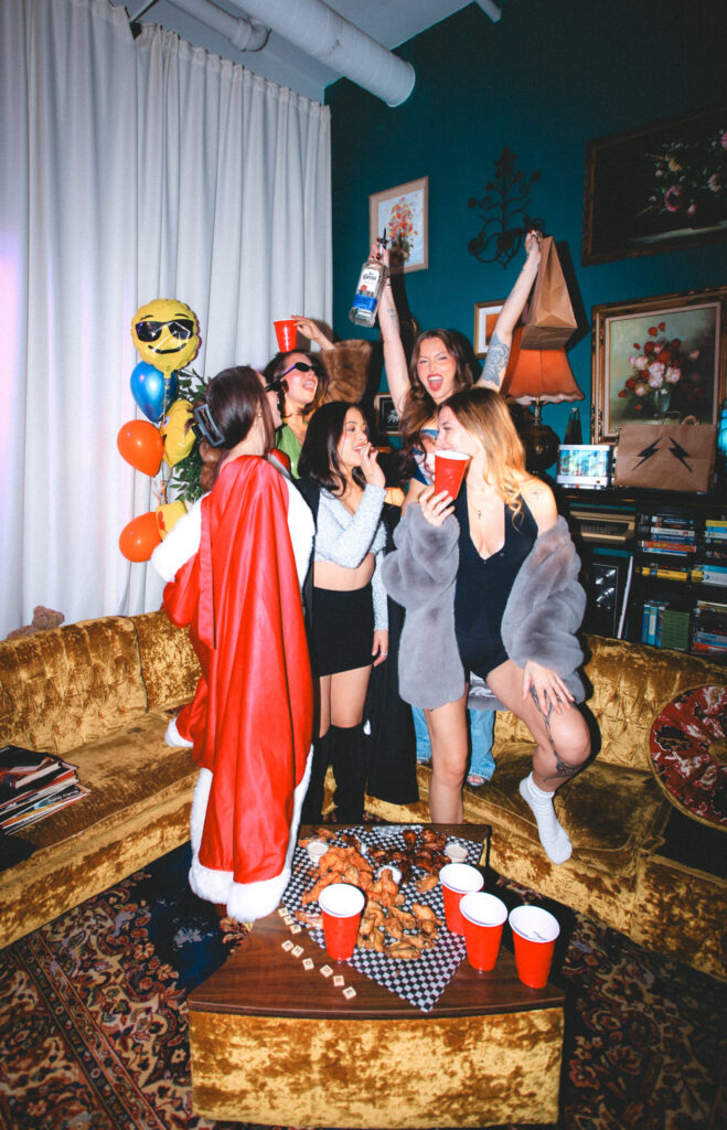 Friends in festive outfits cheering and posing with Warehouse food and drinks during a birthday celebration.