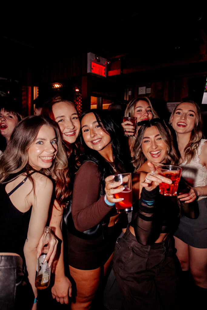 Group of six young women at Warehouse smiling and holding drinks while posing together.