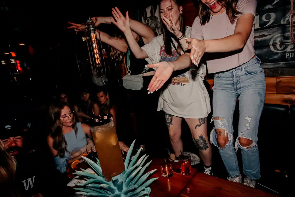 Three women cheering around a large drink tower at Warehouse