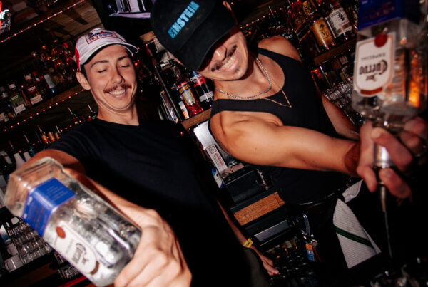 Bartenders at Warehouse pouring vodka into shot glasses behind a lively bar during a World Cup watch party.