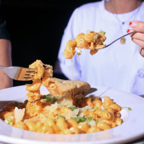 Close-up of Warehouse’s mac and cheese being shared, featuring gooey cheese, green onions, and garlic bread.