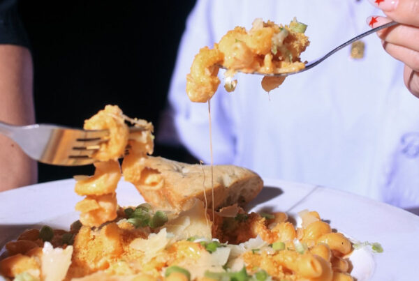 Close-up of Warehouse’s mac and cheese being shared, featuring gooey cheese, green onions, and garlic bread.