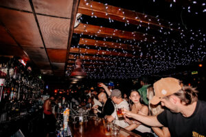 Guests enjoying drinks and conversation inside a lively Warehouse bar featuring a vibrant atmosphere and casual dining setting.