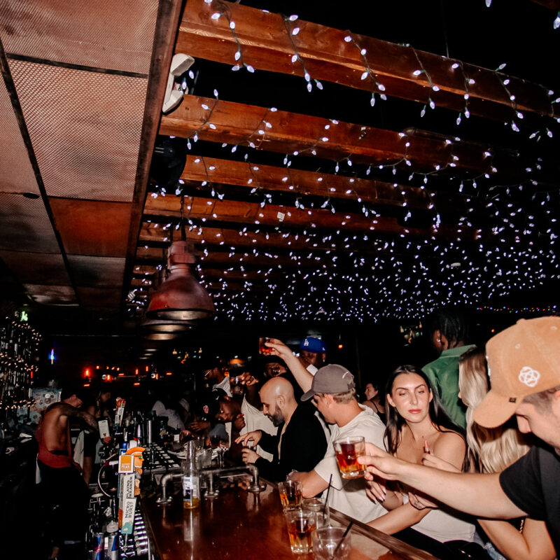 Guests enjoying drinks and conversation inside a lively Warehouse bar featuring a vibrant atmosphere and casual dining setting.