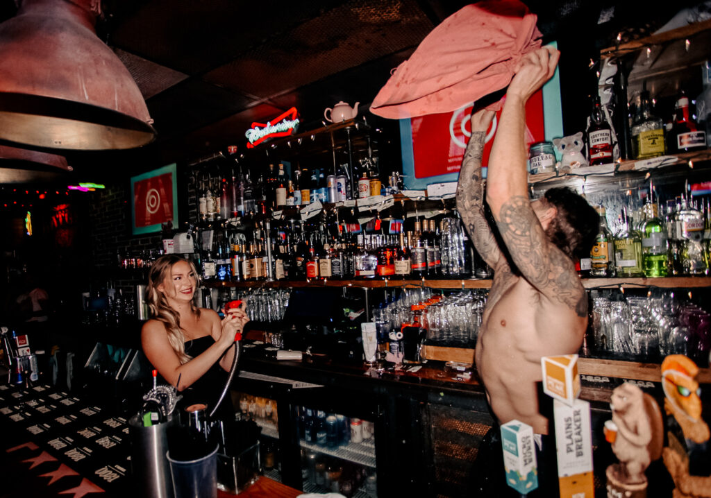 Two smiling Warehouse bartenders preparing cocktails behind the bar during a busy service.
