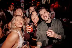 Group of friends smiling and raising cocktails at Warehouse during a lively night out.